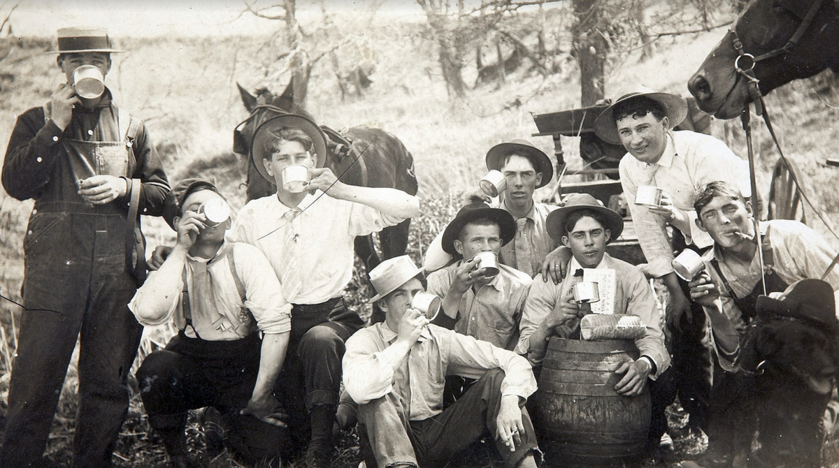 Historic photo of young cowboys drinking coffee beside a barrel